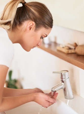 Going through her morning routine. a young woman washing her face in the bathroom.の写真素材