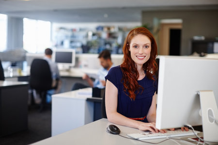 My career is right on track. Portrait of a happy businesswoman using a computer at her work desk.の写真素材