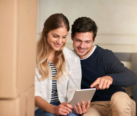 Hey, our new house has great wifi. a happy young couple taking a break with their tablet while moving into their new home.の写真素材
