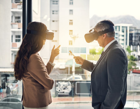 There are many ways to perceive success. two businesspeople wearing VR headsets while working with notes on a glass wall in an office.の写真素材
