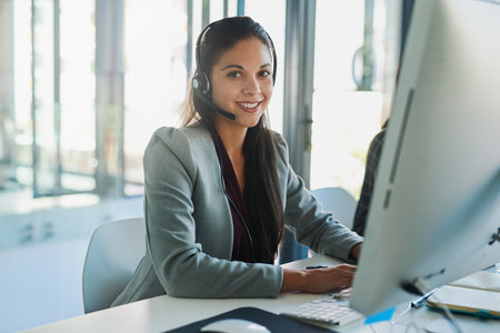 The voice of your company. Portrait of a young woman wearing a headset and using a computer at her work desk.の写真素材