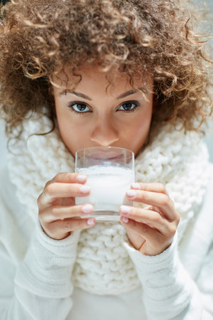 Get your daily dose of mmm. Portrait of a young woman dressed in warm clothing drinking a glass of milk.の写真素材