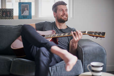 When certain tunes remind you of some great times...a handsome young man playing a guitar at home.の写真素材