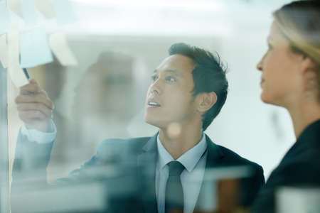 Lets make these ideas happen. coworkers using sticky notes against the wall during a brainstorming session.の写真素材