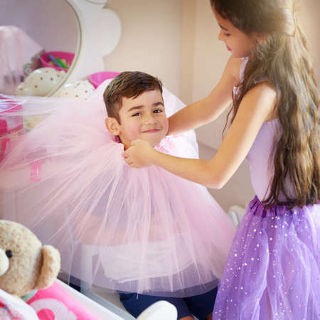 This is what I get for losing a bet. a cute little girl playing dress up with her brother at home.の写真素材
