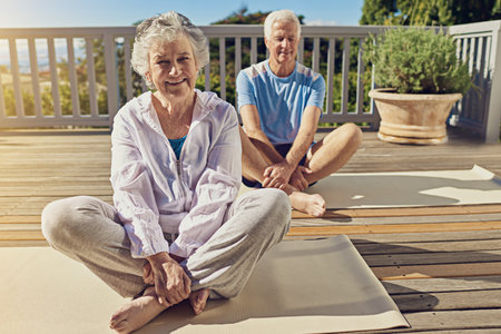 Staying fit and healthy through yoga. Portrait of a senior couple doing yoga together on their patio outside.の写真素材