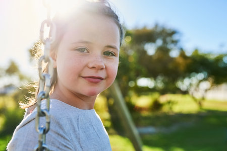 Swinging the day away. Portrait of a cute little girl sitting on a swing in a park.の写真素材