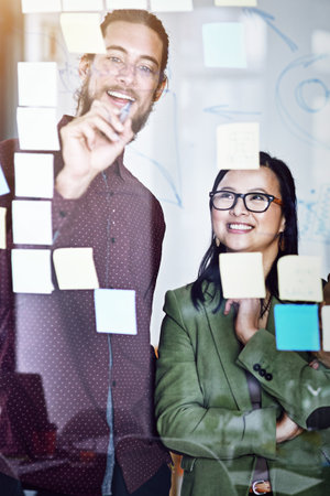 Those who plan, prevail. two businesspeople working on a glass wall the office.の写真素材