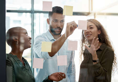 Team strategy meeting on research, post it on glass wall and group work planning together. Business people brainstorming analytics vision think tank ideas, collaboration thinking and sticky notesの写真素材