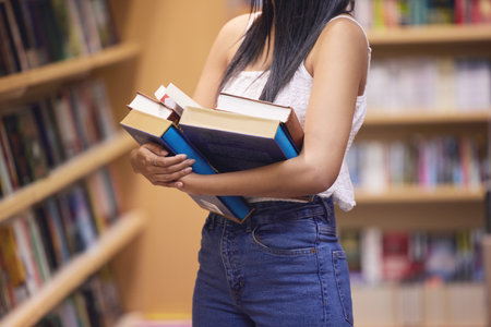 Woman librarian with library print books from shelf for college or university education and learning knowledge. Young student or person with hardback English book in hands for studying or readingの写真素材