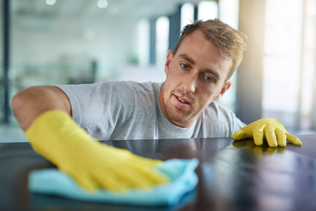 Leaving no trace of dust. a young man wiping off the surfaces in an office.