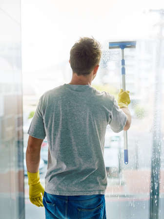 Making sure your view is unimpaired. Rearview shot of a young man cleaning the windows in the office.の写真素材