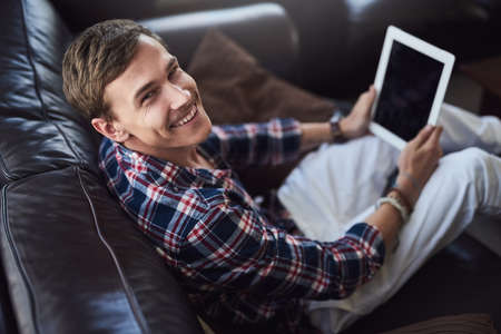 Im getting into the whole blogging thing. High angle portrait of a handsome young man using his laptop while sitting on the sofa at home.の写真素材