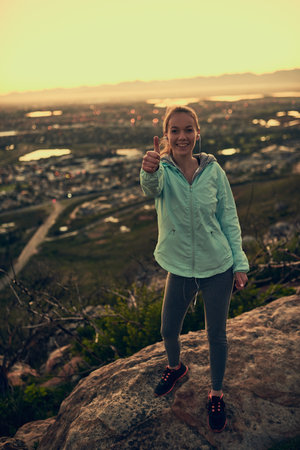 My progress is simply positive. Portrait of a sporty young woman giving you thumbs up during a hike up the mountain.の写真素材