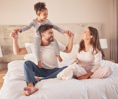 Happy family while playing and fun in bed at home together in the morning. Mother, father and girl or daughter laughing and playful fun with love in the bedroom at home while bonding togetherの写真素材