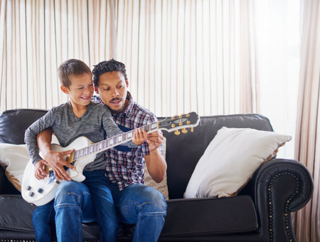 Teaching his son a new tune. a father teaching his son how to play guitar at home.の写真素材