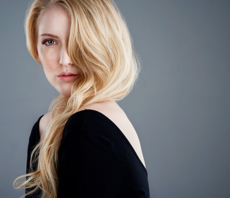 Gorgeously golden tresses. Studio portrait of an attractive young woman with beautiful blonde hair posing against a gray background.の写真素材