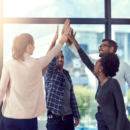 Go team. a group of people high fiving in the office.の写真素材