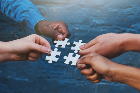 Finding solutions piece by piece. four people each holding a puzzle piece to fit together.の写真素材