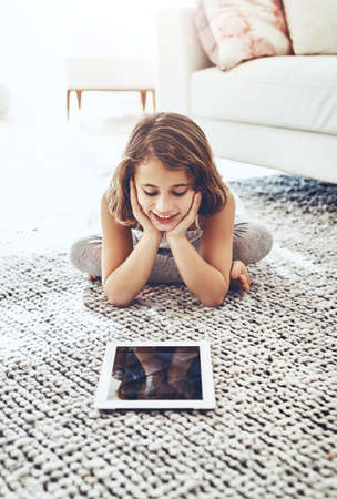 Cute and carefree. a cute little girl using a digital tablet while relaxing at home.の写真素材