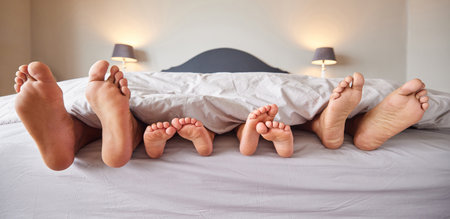 Feet of family relax in bed, sleeping and lying together in bedroom at home. Tired parents being lazy with children, sleeping in on the weekend, cozy and comfortable, sharing comfort with kidsの写真素材