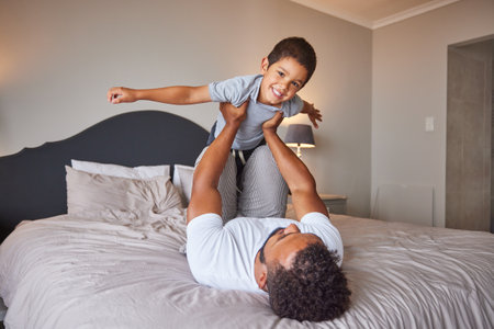 Smile, love and happy father and son family time playing in bedroom bed lifting him like airplane or superhero. Loving dad, man or single parent bonding with cheerful kid in the morning at home.の写真素材