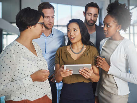 I can show you...a group of businesspeople looking at a tablet in the office.の写真素材