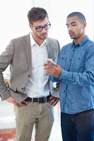 Let me show you this app. two male colleagues discussing something on a cellphone.の写真素材