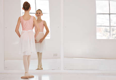 Young ballet dancer dancing in studio, doing dance performance before competition and learning creative sport in mirror at school. Girl ballerina training her balance and child in start positionの写真素材