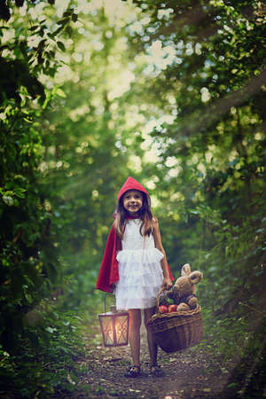 Im off to visit Grandma in the woods. a little girl holding a lantern and a basket in the woods.の写真素材