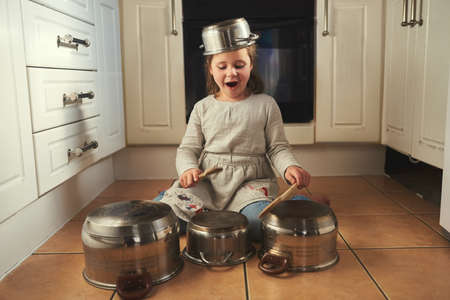 Time for a drumroll. a little girl playing drums on a set of pots in the kitchen.の写真素材