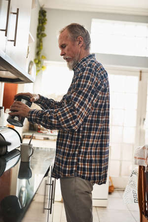 Time to start the day with a great cup of coffee. a focused senior man making himself a cup of coffee in the kitchen at home.の写真素材