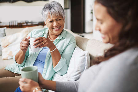 Did she really. a young woman and her mother catching up on the sofa while drinking coffee.の写真素材
