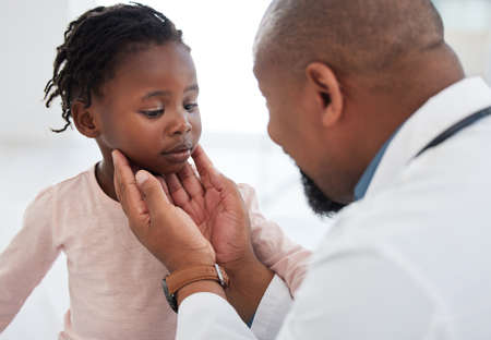 Medical doctor checking a girl throat with care in his office at a modern surgery center. Man pediatrician touching the patients neck during healthcare, medicare and illness consultation at clinicの写真素材