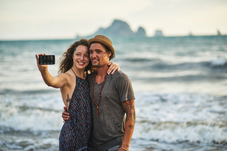Beach hair, dont care. a happy young couple taking a selfie while posing on the beach.の写真素材