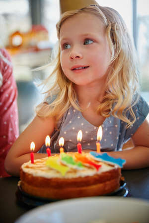 Do I get to have the biggest slice. an adorable little girl sitting in front of her birthday cake.