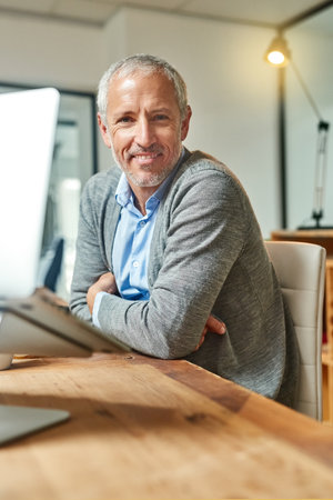 This is where I do my best work. Portrait of a smiling mature businessman sitting at his desk in an office.の写真素材