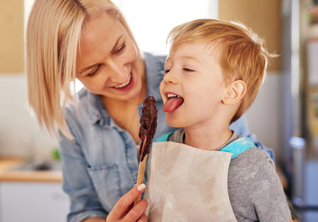 The best part about baking is licking the spoon. a mother giving her son a spoon of chocolate batter to lick from.の写真素材