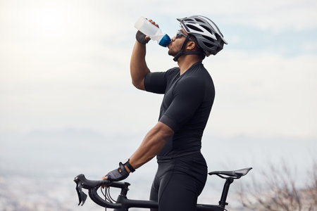 Sports man with a bike drinking water bottle doing fitness training or workout on sky mockup background. Healthy, professional athlete cyclist with a bicycle during cycling cardio exercise in natureの写真素材