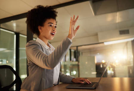 Surprised, shocked and excited business woman by a virtual or digital screen in an office while typing on a laptop. A female employee working late at night is amazed by a hologram at the workplaceの写真素材