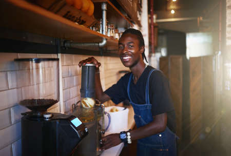 Freshly squeezed juice coming right up. a young man using a juicer in a coffee shop.の写真素材