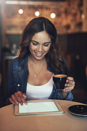You guys should check out this coffee spot. a relaxed young woman using her tablet in a coffee shop.の写真素材