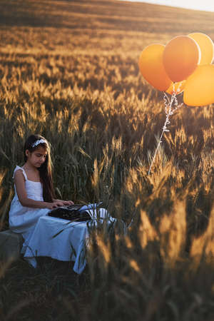 Nature is a source of unending inspiration. a cute little girl playing with a typewriter while sitting in a cornfield.の写真素材