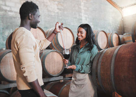 Wine tasting, couple and distillery farm worker serving red alcohol drink in glass with pipette in countryside. Happy smile, learning man and woman or winery waiter on sustainability luxury vineyardの写真素材