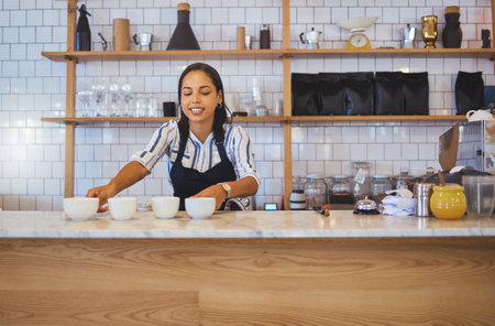 Coffee shop, employee or worker of a woman in a retail business handing warm beverages on a counter at a cafe. Barista serving ready drinks on a table from orders for waiter or waitress to serve.の写真素材