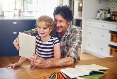 Theres so much to learn online. a father helping his daughter complete her homework on a digital tablet.の写真素材