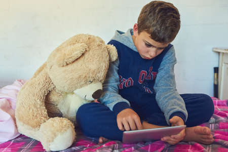 Teddy is just as curious about technology. a young boy using a digital tablet at home.の写真素材