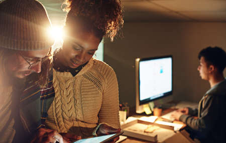 Technology will make night shift shorter. two coworker discussing something on a digital tablet while working night shift at the office.の写真素材