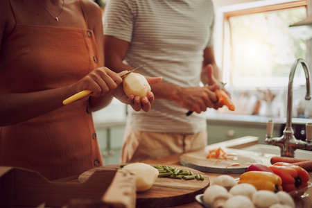 Health, diet and food of a couple cooking a meal together for lunch in the kitchen at home. Man and woman in a relationship working as a team to cook fresh organic vegetables for healthy nutrition.の写真素材