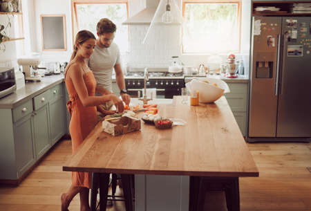 Couple cooking, home food or healthy meal for bonding, happy or fun man and woman in house kitchen together. Conversation, love or young people in modern interior with fresh salad vegetables on tableの写真素材
